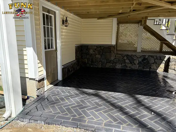 Finished paver patio beneath a deck with stone wall, built by Funk Landscape & Design